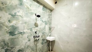 Un baño con pared de mármol, ducha, lavamanos e inodoro.