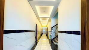 A hotel hallway with a marble floor, a staircase with metal railings, and a ceiling with recessed lighting.