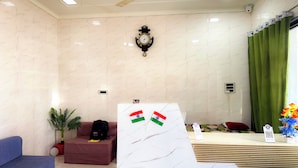A reception area with a marble wall, a clock, a ceiling fan, a reception desk, a plant, and a sofa. - Vimla Residency Hotel Near Prem Mandir (Vrindavan)