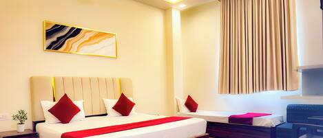 A hotel room with a large bed, a bedside table with a plant, a small desk, and a window with curtains.