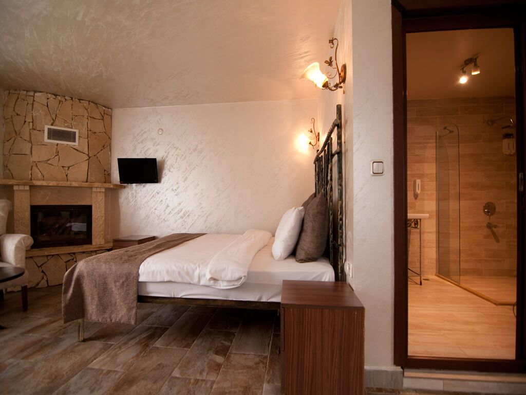 A bedroom with a stone fireplace, a bed with pillows, a bedside table, and a wooden bench.