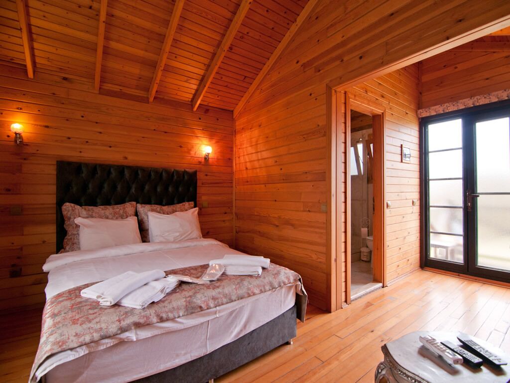 Une chambre dans une cabane en bois, avec un lit, une table de chevet et une porte donnant sur un balcon.