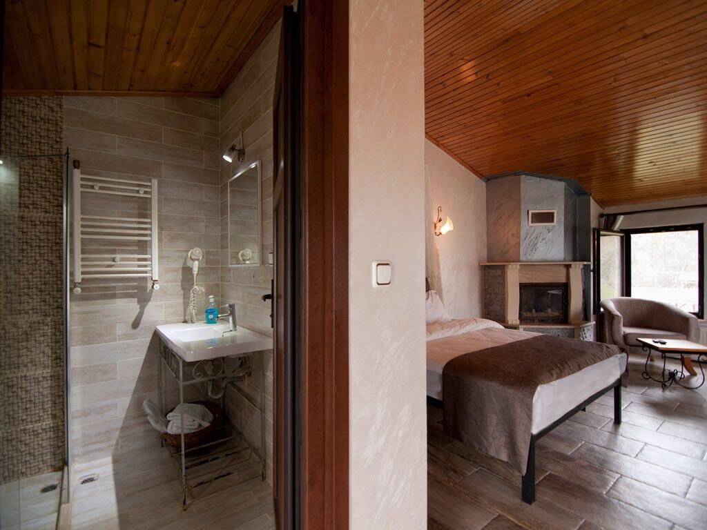 Un baño moderno con ducha, inodoro y lavamanos. Hay una cama con cabecero y una mesita con una silla.