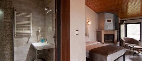 Un baño moderno con ducha, inodoro y lavamanos. Hay una cama con cabecero y una mesita con una silla.