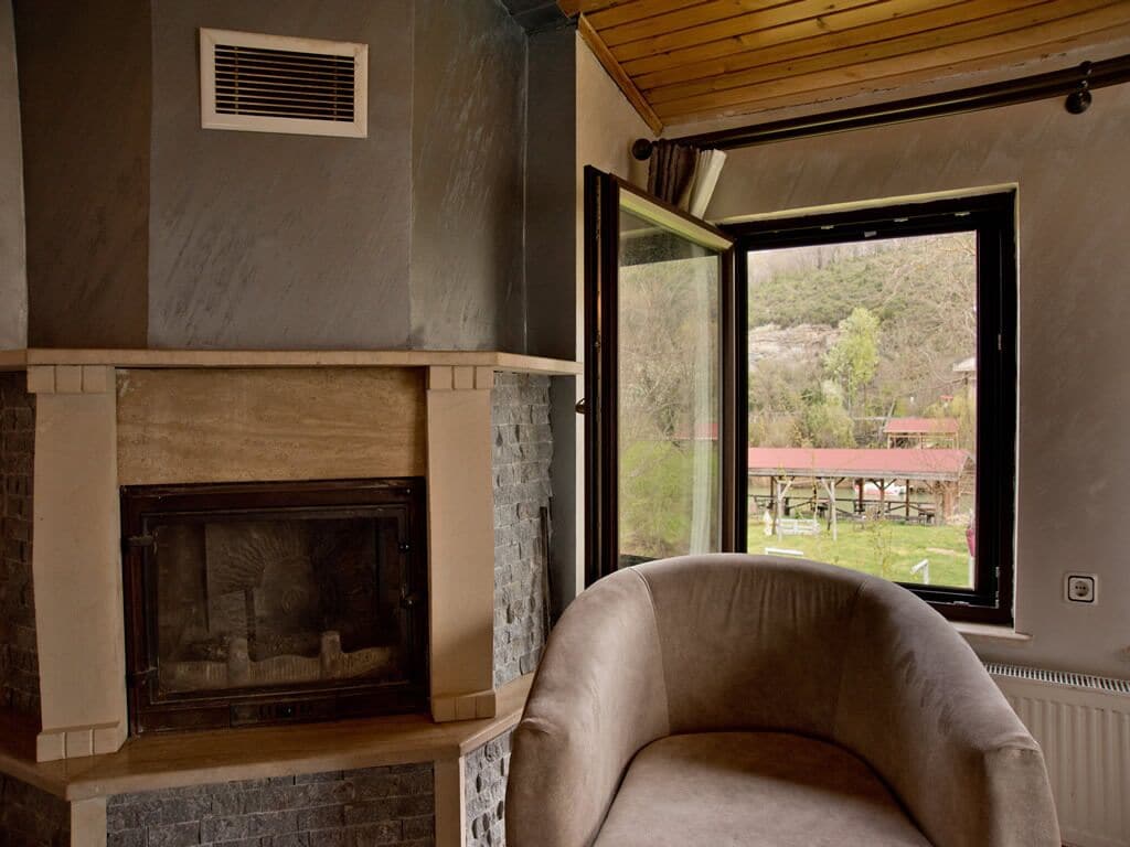 A room with a fireplace, a comfortable armchair, and a large window offering a view of the outdoors.