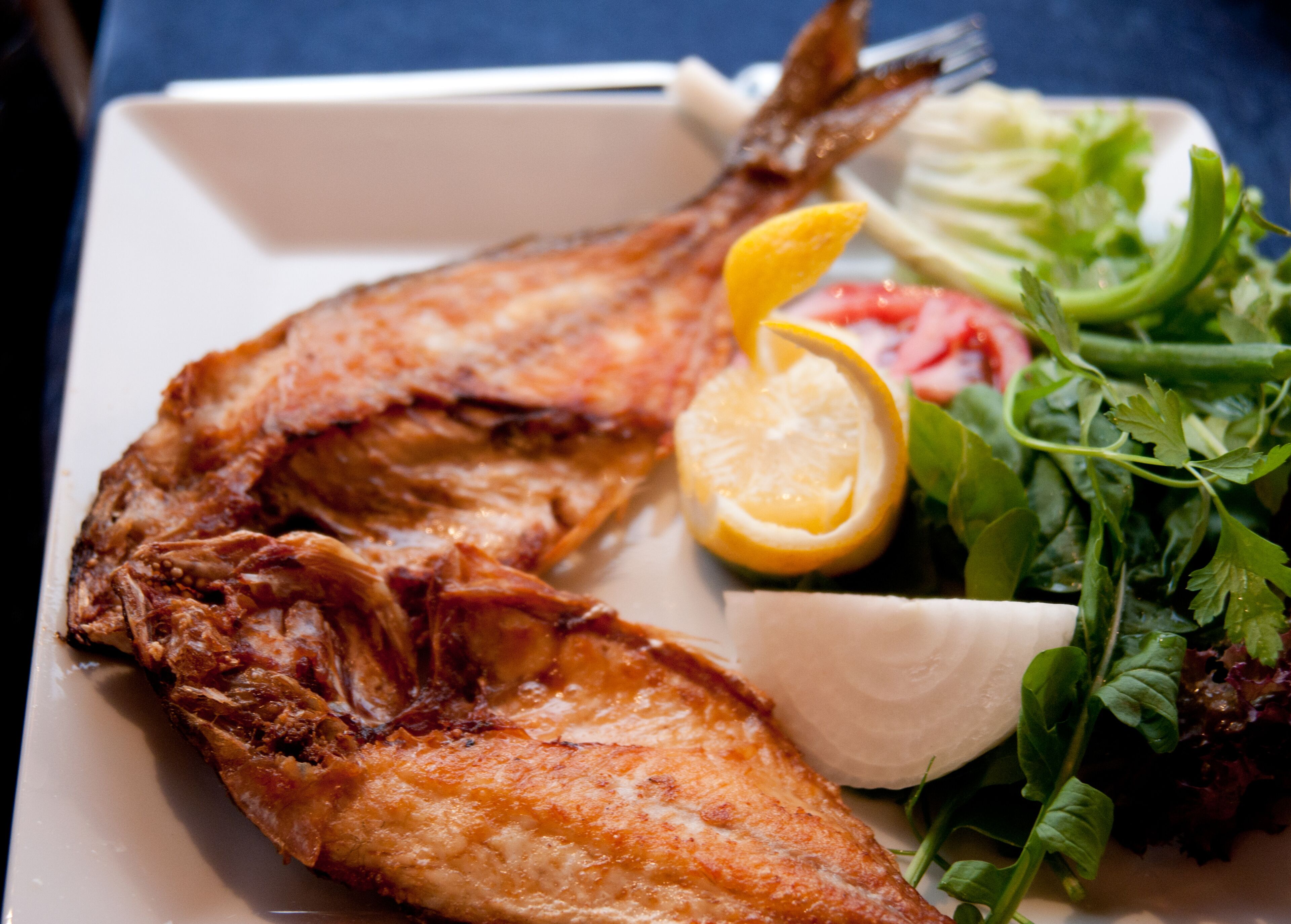 A plate with a whole fried fish, lemon slice, and a side salad.