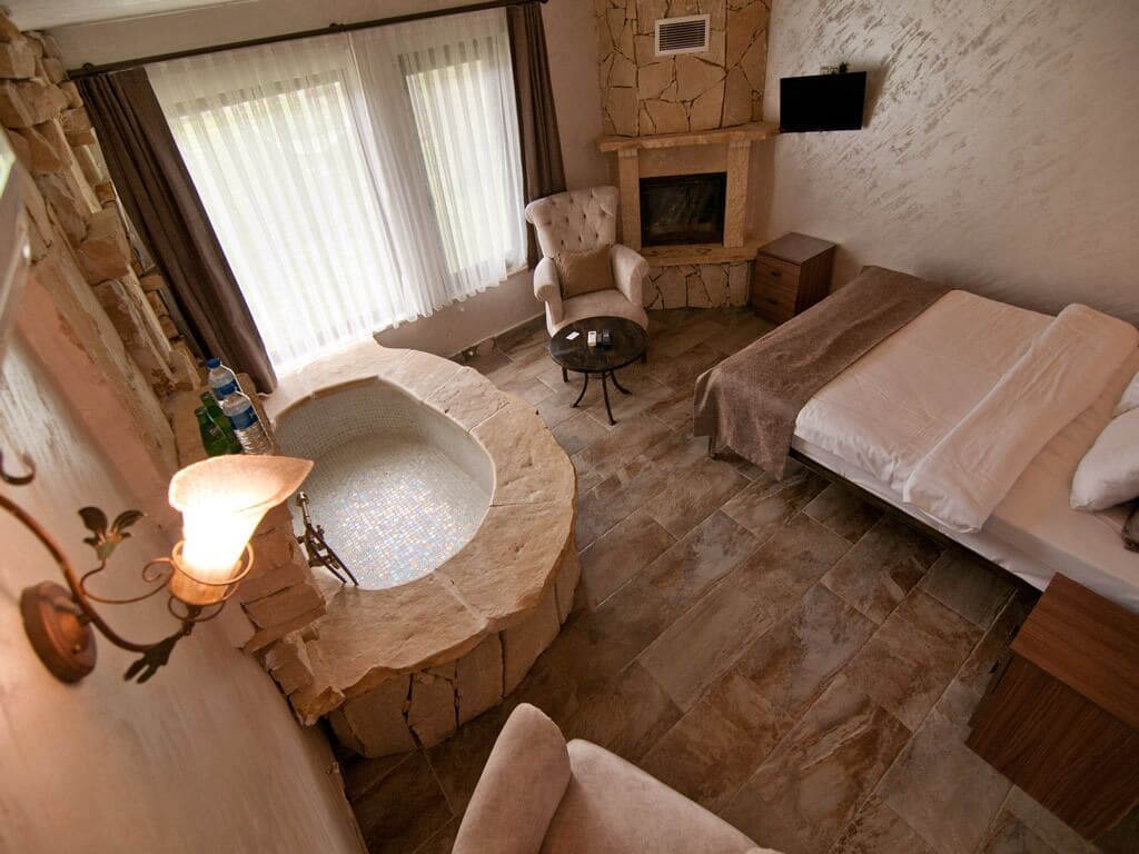 A room with a stone fireplace, a round bathtub, a sofa, and a bed.