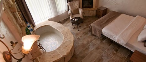 A room with a stone fireplace, a round bathtub, a sofa, and a bed.