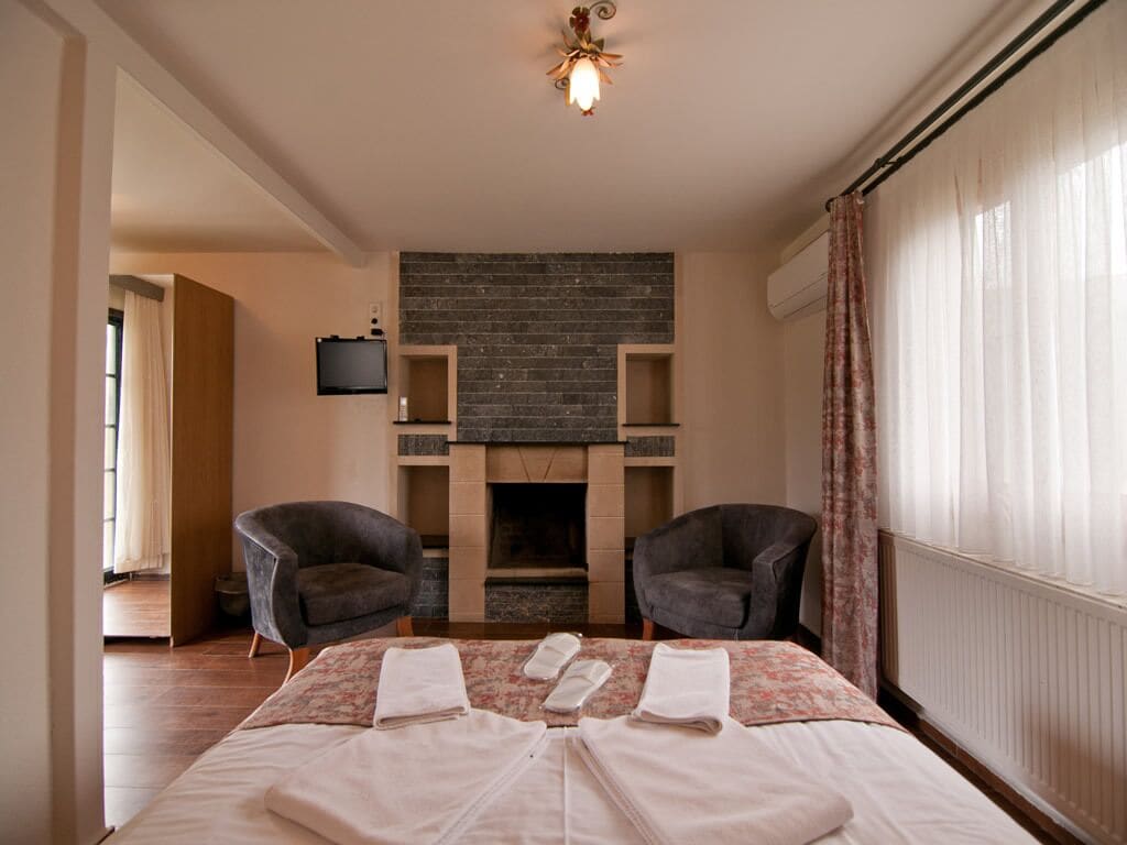 Una habitación de hotel con una cama, dos sillones, una chimenea y un televisor.