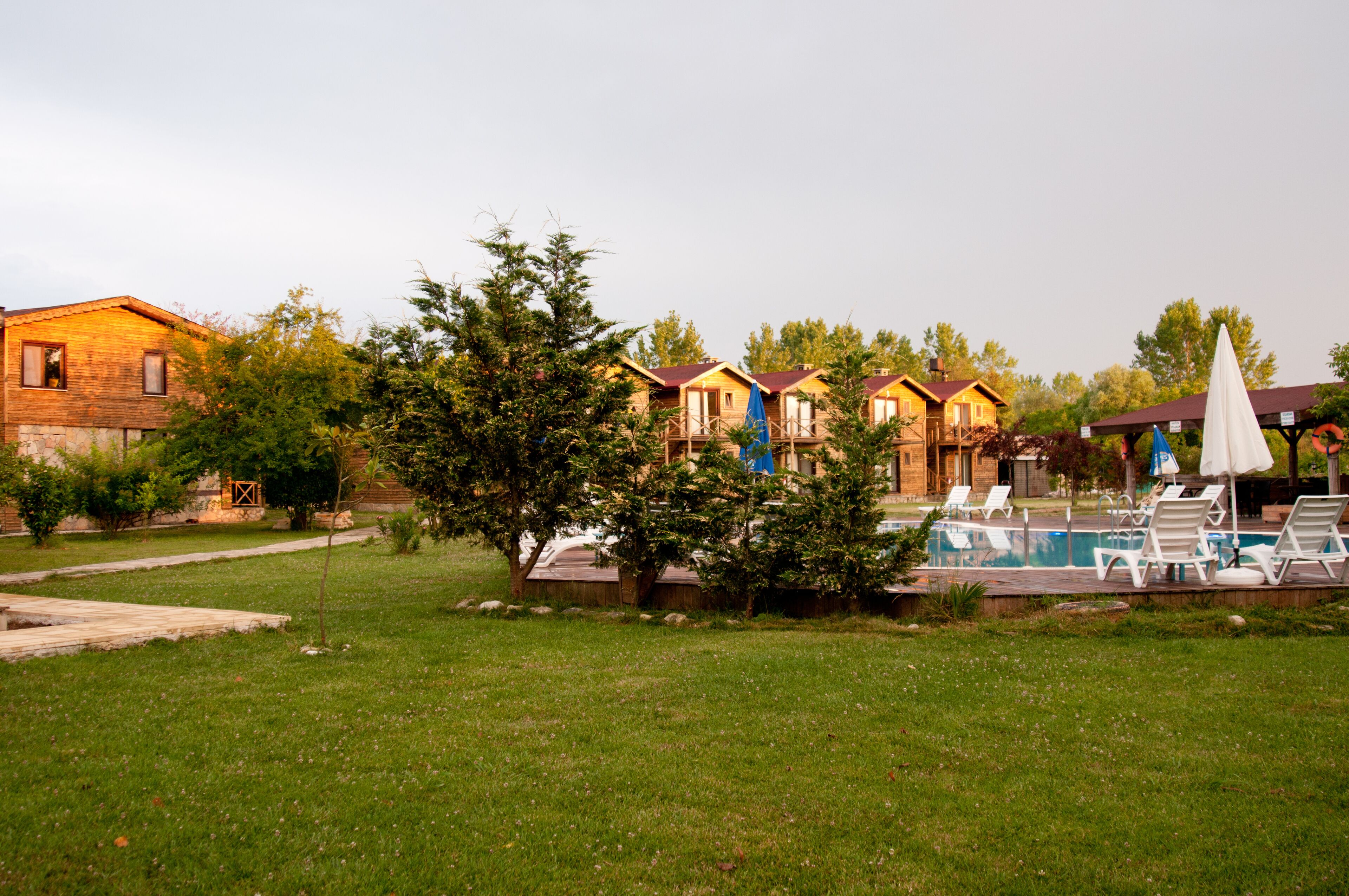 A row of wooden cabins with a swimming pool and lounge chairs.