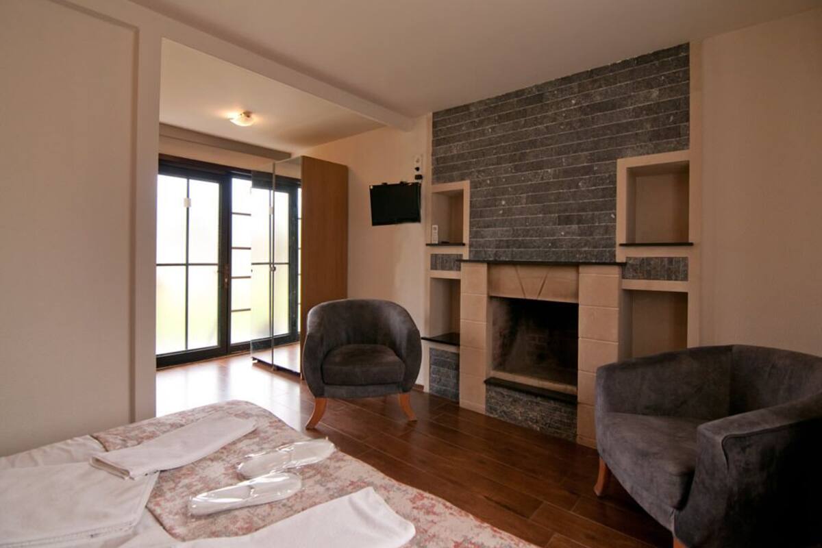 A living room with a fireplace, two armchairs, a flat-screen TV, and a large window.
