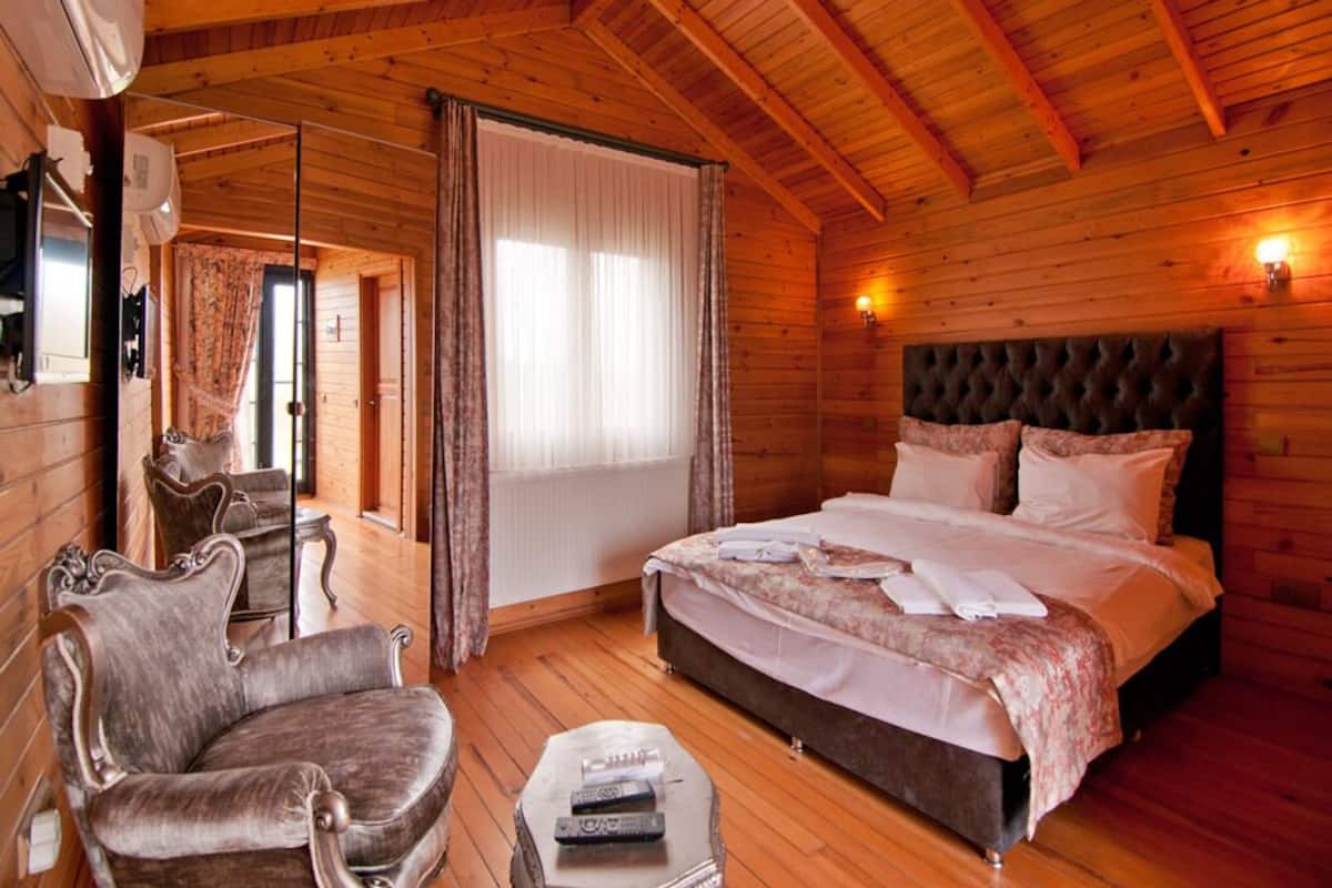 A wooden-paneled bedroom with a large bed, a chair, and a small table.