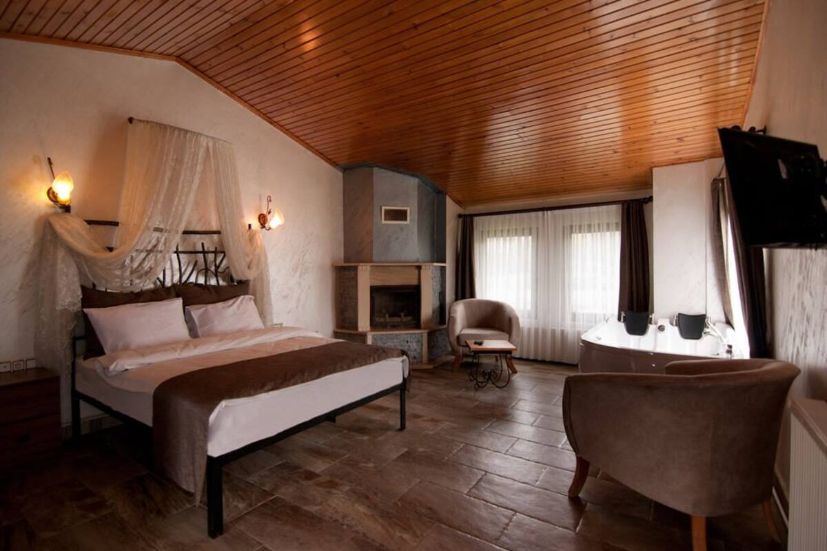 A bedroom with a wooden ceiling, a bed, a chair, a small table, and a fireplace.