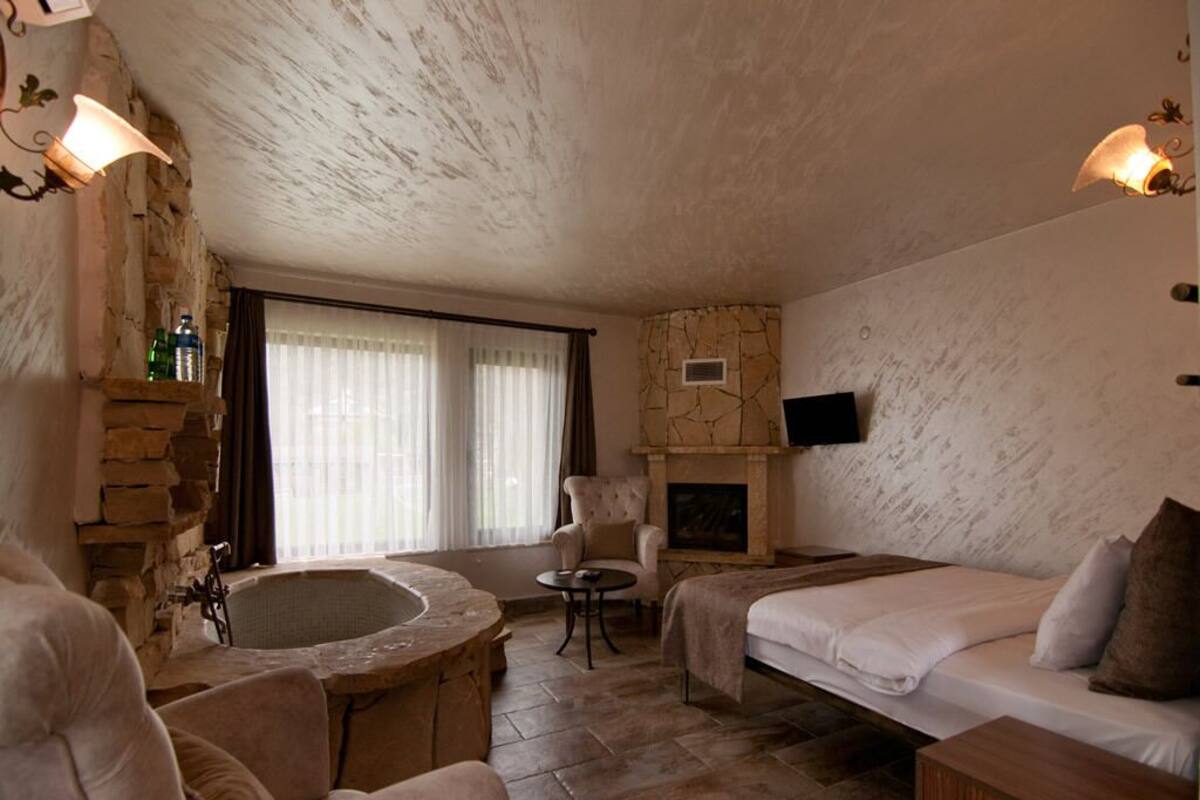 A cozy room with a stone fireplace, a large window with curtains, a sofa, a chair, and a small table.