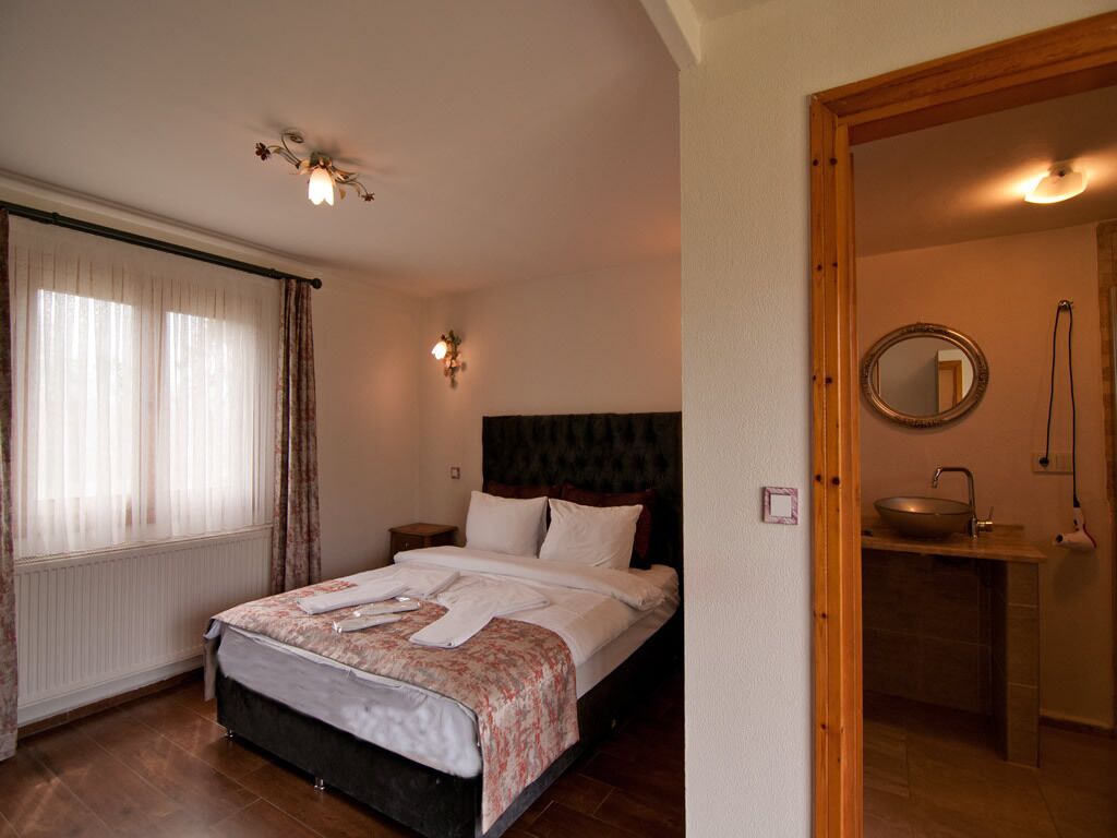 Un dormitorio con cama, una mesita de noche, un espejo y un baño con lavabo y espejo redondo.