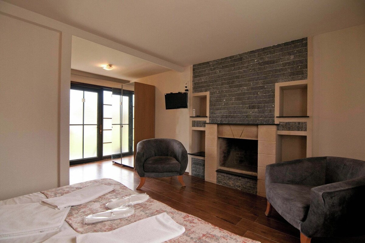 A living room with a fireplace, two armchairs, a sofa, and a large window.