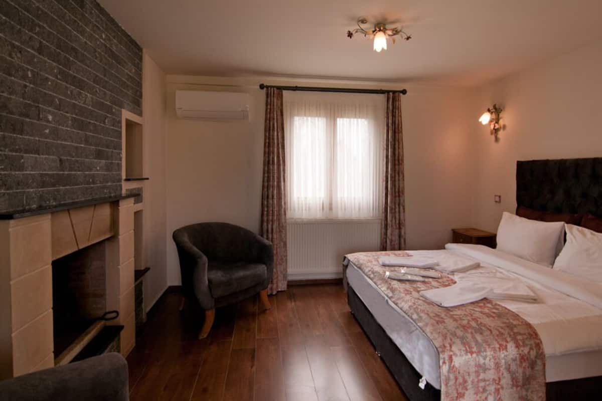 A bedroom with a bed, a chair, a fireplace, and a window with curtains.