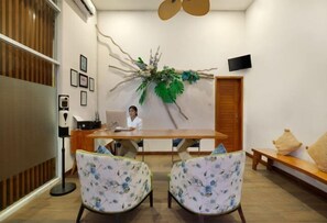 A room with a wooden table, two floral chairs, a decorative wall piece, a television, and a wooden door. - The Luxury Collection, Monaco Blu (Bali)