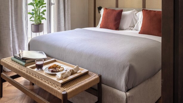 Habitación de hotel ordenada con cama, mesita de noche y una planta en maceta.