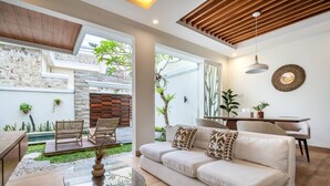 A modern living room with a sofa, coffee table, and chairs. There is a dining table with chairs and a decorative wall piece. - Orivista NEW! Luxe Private Pool Villa w Rooftop (Mengwi)