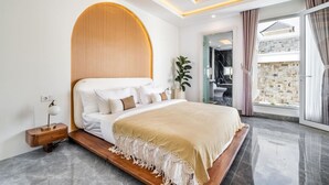 A modern bedroom with a large bed, a wooden headboard, a nightstand, a bedside lamp, and a view of the bathroom and outdoor area. - Orivista NEW! Luxe Private Pool Villa w Rooftop (Mengwi)