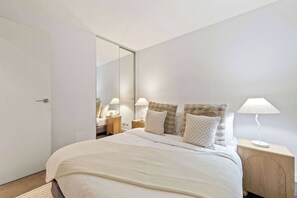 Un dormitorio moderno con una cama grande, una mesita de noche con lámpara y un espejo en la pared.