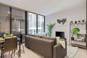 Una sala moderna con sofá, mesa de comedor, sillas, televisor y plantas en macetas.