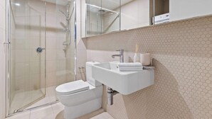 Een moderne badkamer met een douchecabine van glas, een witte wastafel en een toilet.