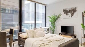 Een moderne slaapkamer met een groot bed, een bureau, een stoel, een televisie en een plant.