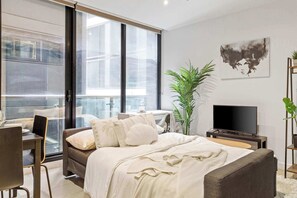 Une chambre moderne avec un grand lit, un bureau, une chaise, une télévision et une plante.