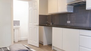 Una cocina compacta con armarios blancos, encimera negra y un lavamanos visible.