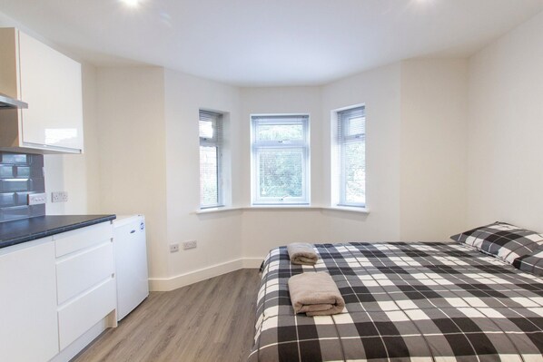 A bedroom with a bed, a small kitchenette, and three windows.