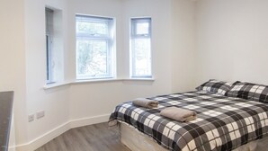 Un dormitorio con una cama, dos ventanas y un radiador en esquina.