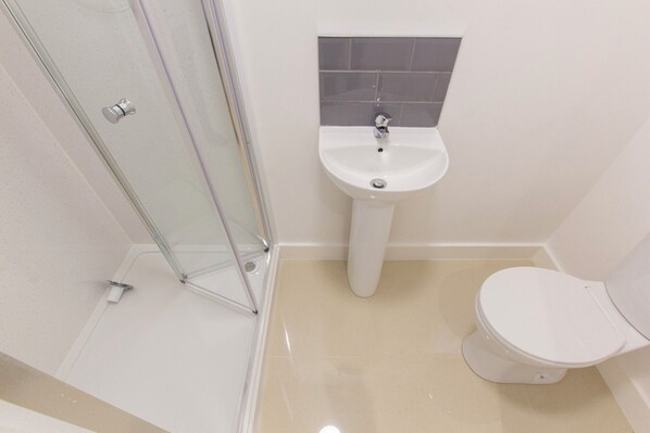A bathroom with a glass shower enclosure, a pedestal sink, and a toilet.