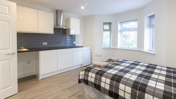Un dormitorio compacto con cama, kitchenette pequeño y ventana.