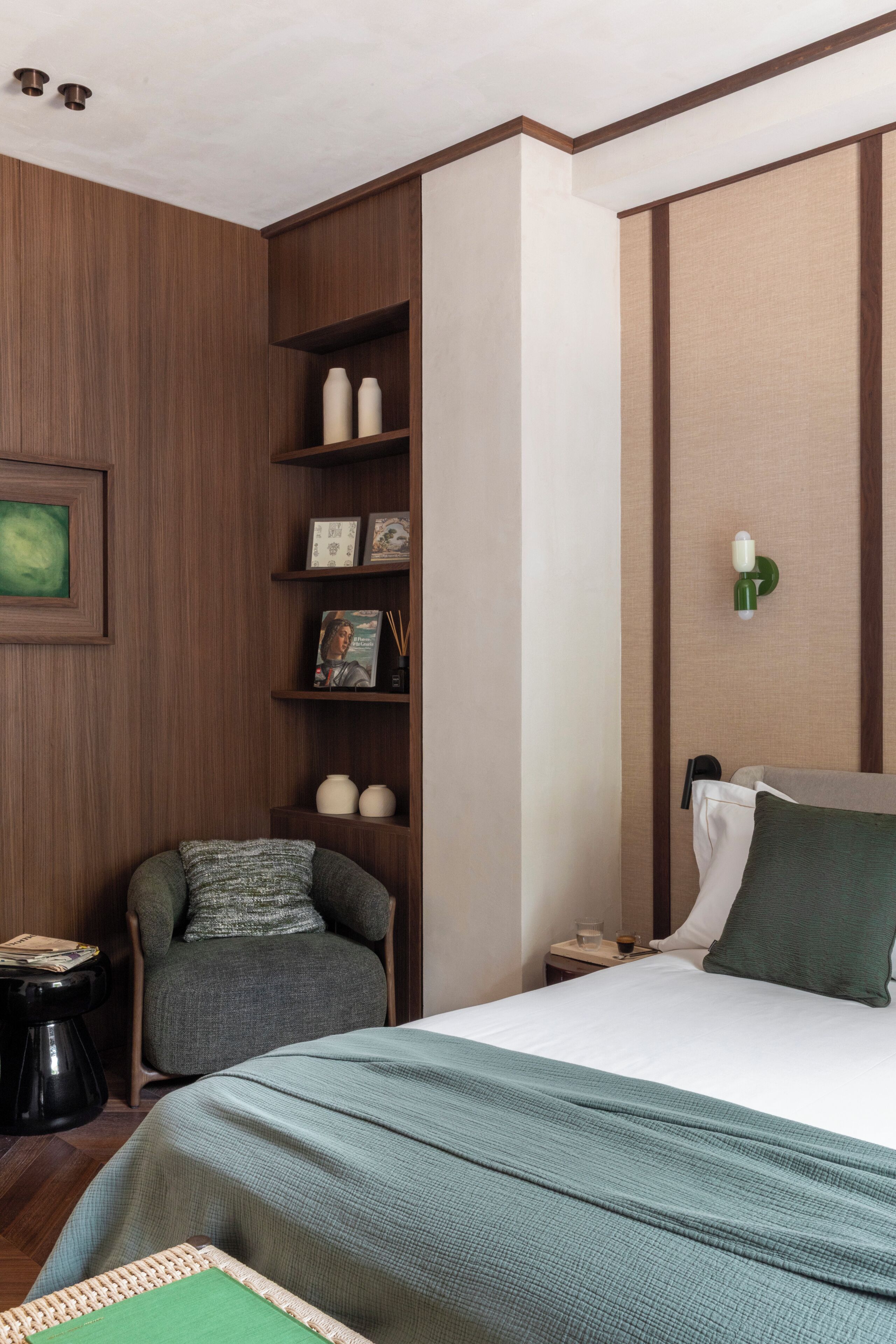 A bedroom with a bed, a chair, a nightstand, and a wall-mounted shelf with decorative items.