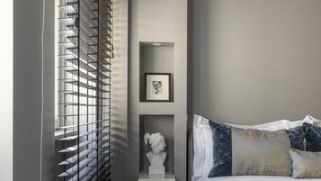 A bedroom with a bed, a nightstand, a framed picture, and a window with blinds.