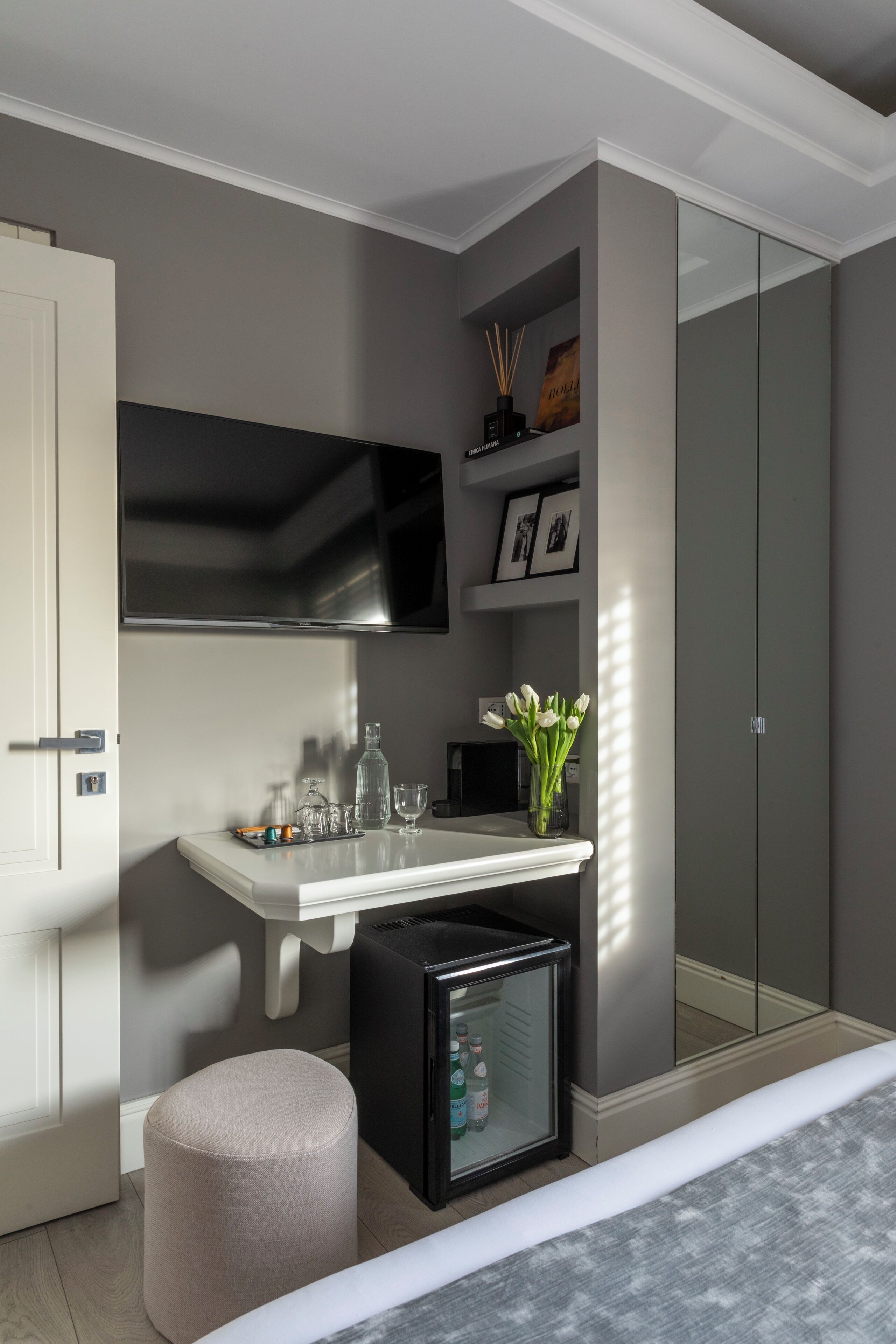 A modern bedroom with a bed, a bedside table, a TV, a wardrobe, and a small fridge.