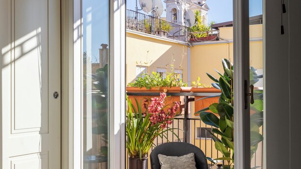 A balcony with a view of a building with domed structures, a chair, and potted plants. - Naman Hotellerie - Condotti (Rome)