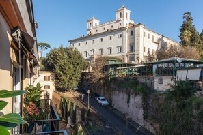 A building with a prominent bell tower, a narrow street with parked cars, and a balcony with plants. - Naman Hotellerie - Condotti (Rome)