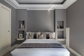 A bedroom with a large bed, grey walls, and white trim. There are shelves with decorative items and a framed picture on the wall. - Naman Hotellerie - Condotti (Rome)