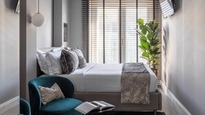 A bedroom with a bed, a chair, a plant, and a window with blinds. - Naman Hotellerie - Condotti (Rome)