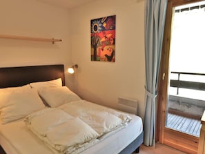 Ein Schlafzimmer mit einem Bett, einer Wandleuchte, einem Fenster mit Vorhängen und einem Gemälde an der Wand.