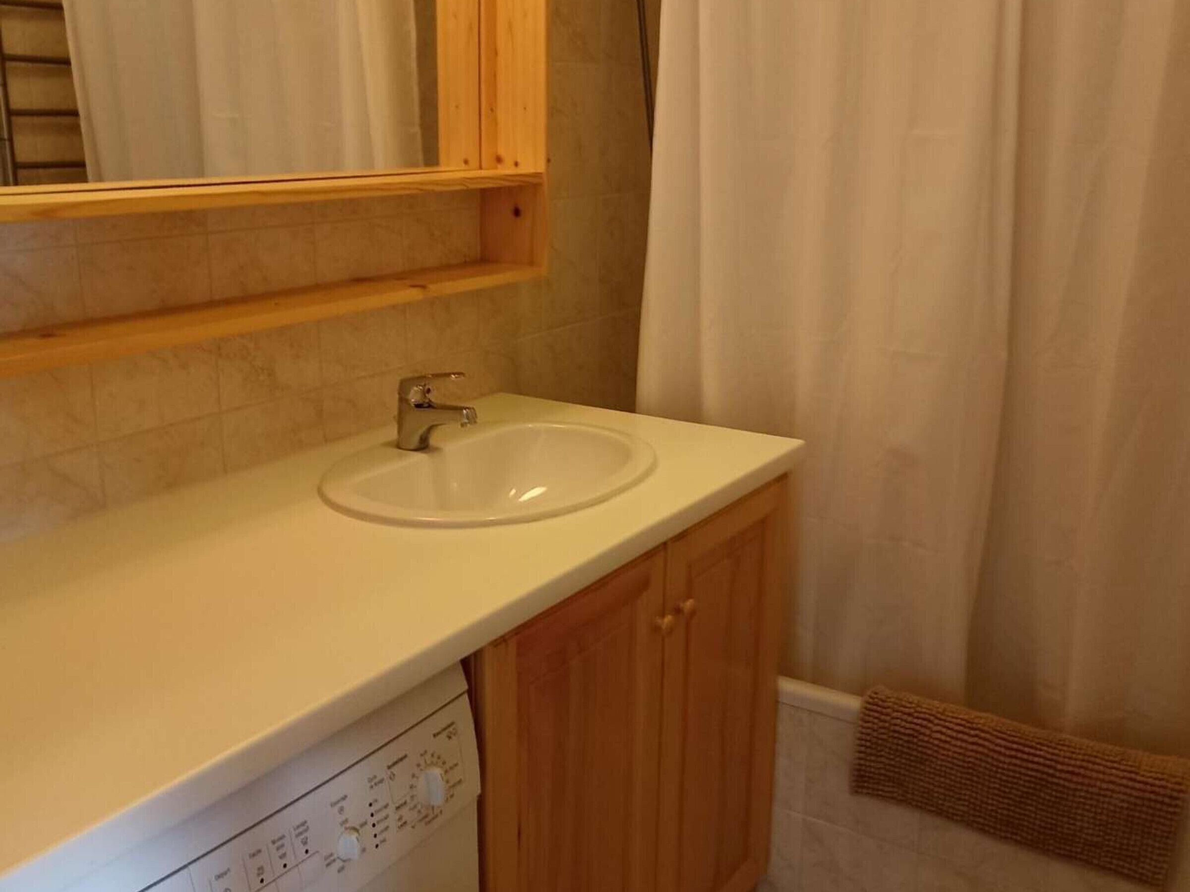 Une salle de bain avec un lavabo blanc, des meubles en bois, un miroir et un rideau de douche.