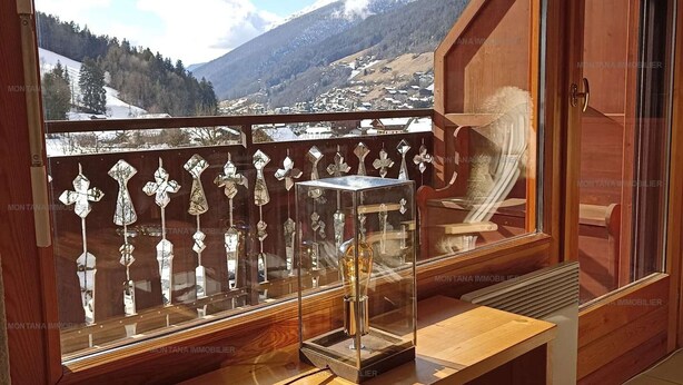 Een balkon met houten hekwerk, een glazen vitrine en uitzicht op een bergachtig landschap.