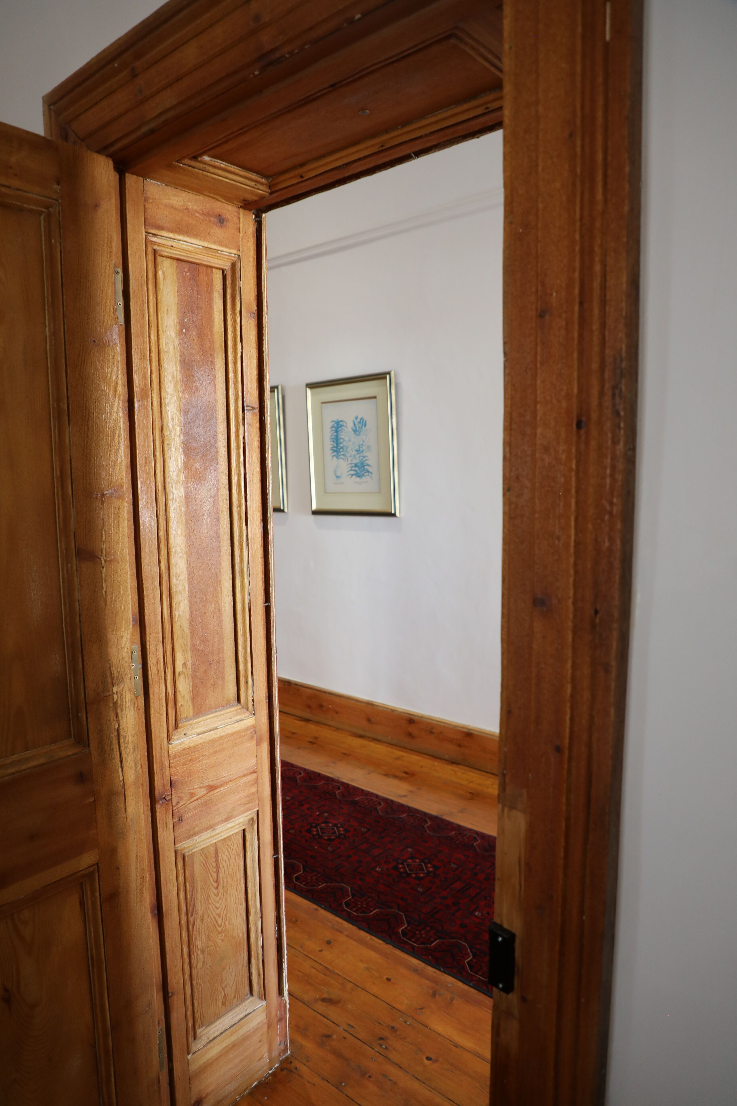 A wooden door leading to a hallway with a red carpet and a framed picture on the wall.