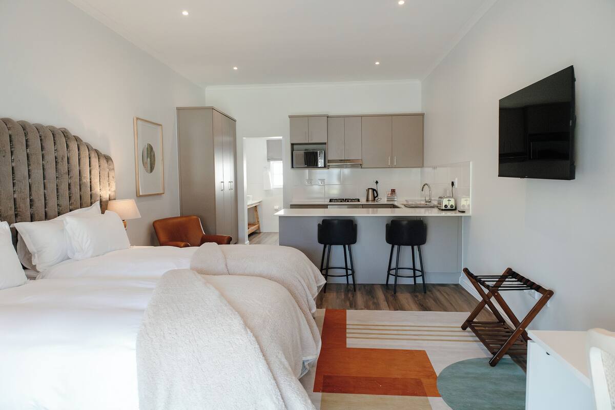Ein modernes Hotelzimmer mit einem großen Bett, einer kleinen Küchenzeile und einem an der Wand befestigten Fernseher.