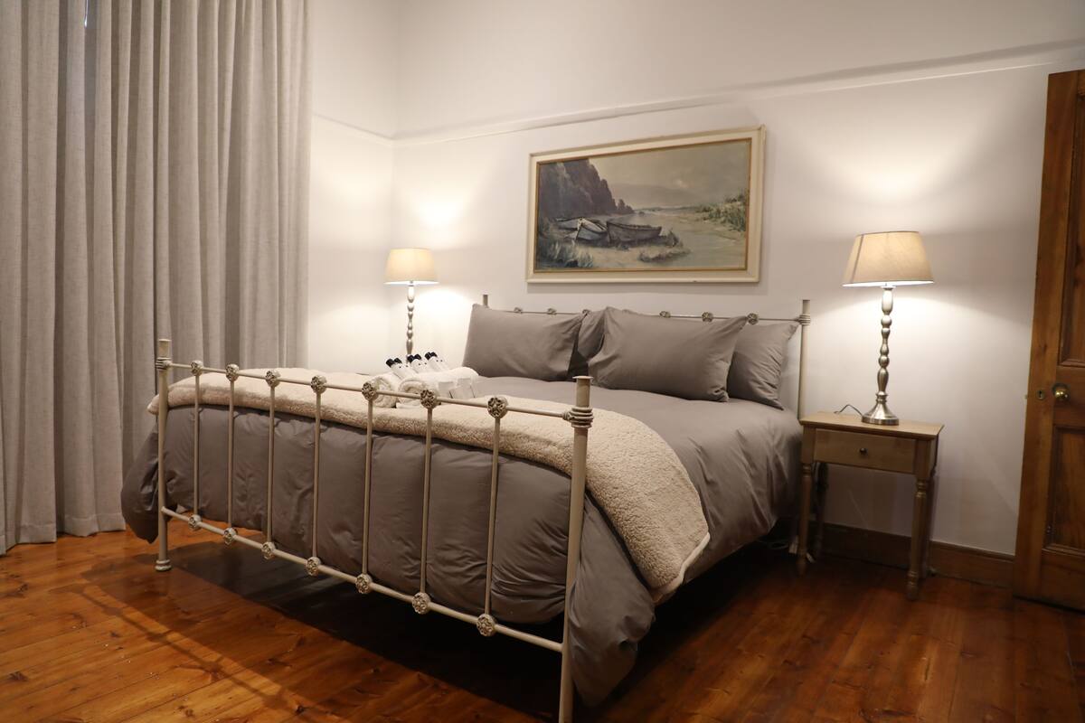 Ein ordentlich eingerichtetes Schlafzimmer mit einem Metallbettgestell, einem Gemälde an der Wand und zwei Nachttischlampen.