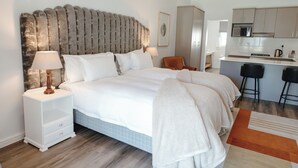 Un dormitorio moderno con una cama grande, mesitas de noche, una silla y una zona de kitchenette.