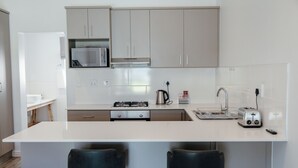 Una cocina moderna con armarios blancos, un microondas de acero inoxidable, una estufa a gas y un tostador. Hay dos taburetes negros en la isla.